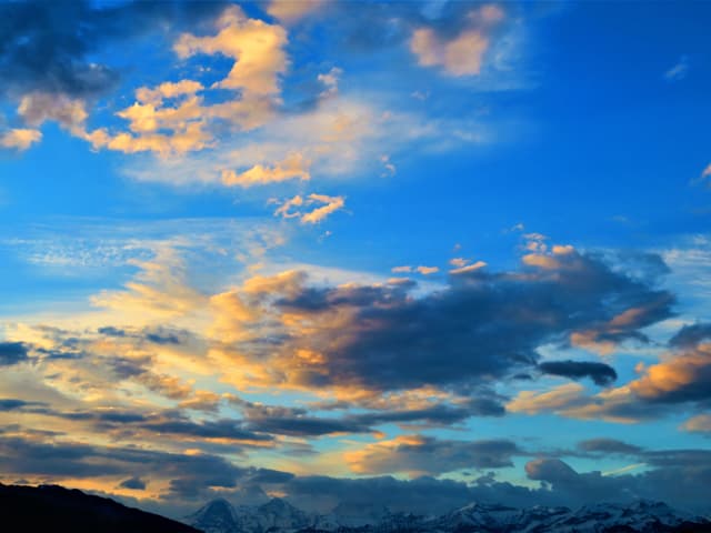 Die Wolken über den Berner Alpen werden gelblich und rötlich eingefärbt. Der Himmel ist strahlend blau.