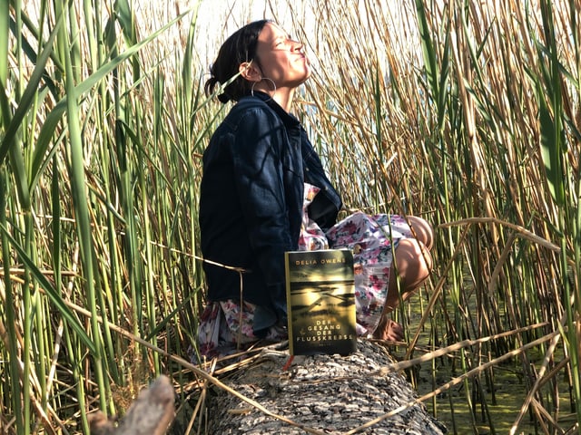 Annette König sitzt im Schilf. Vor ihr auf einem Baumstamm steht der Roman «Der Geang der Flusskrebse» von Delia Owens Annette König sitzt im Schilf. Vor ihr auf einem Baumstamm steht der Roman «Der Geang der Flusskrebse» von Delia Owens