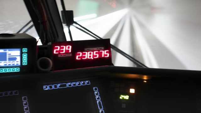 Eine LCD-Anzeige zeigt die Geschwindigkeit des Zuges an und durch die Scheiben des Führerstands sieht man einen hell erleuchteten Tunnel.