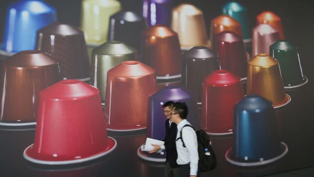 Zwei Asiaten stehen vor einem Plakat. Es zeigt riesige Nespresso-Kapseln. Zwei Asiaten stehen vor einem Plakat. Es zeigt riesige Nespresso-Kapseln.