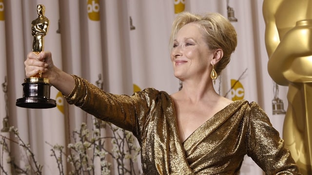 Meryl Streep lächelt und hält mit der rechten Hand den Oscar hoch. Meryl Streep lächelt und hält mit der rechten Hand den Oscar hoch.