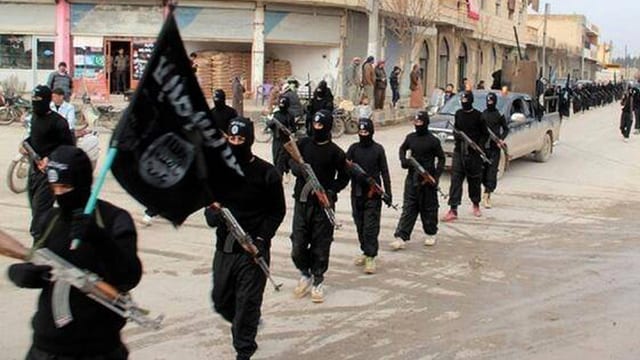 Schwarz gekleidete, vermummte und bewaffnete Dschihadisten defilieren auf einer Strasse. Schwarz gekleidete, vermummte und bewaffnete Dschihadisten defilieren auf einer Strasse.