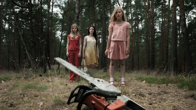 Filmszene: Drei Frauen stehen im Wald neben einer am Boden liegenden Motorsäge.
