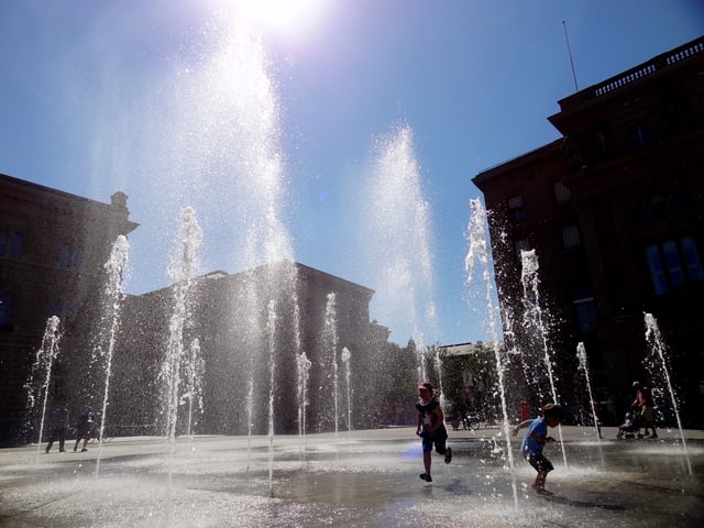 Kinder tanzen auf dem Bundesplatz durch die Fontänen des Wasserspiels.