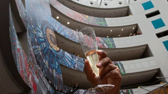 Eine Person hält ein Champagnerglas in die Höhe im Cern-Foyer. Eine Person hält ein Champagnerglas in die Höhe im Cern-Foyer.