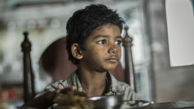 Saroo sitzt an einem Tisch und isst. Saroo sitzt an einem Tisch und isst.