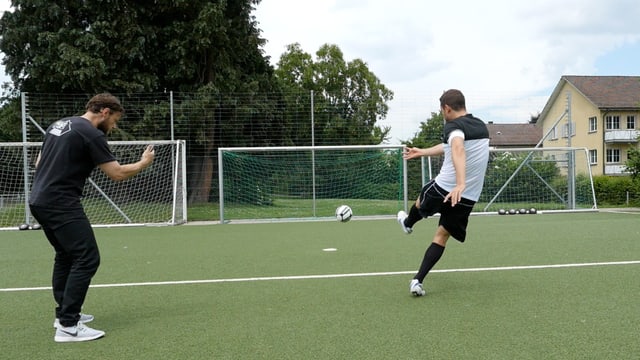 Ein Mann schiesst einen Fussball in ein Tor, ein anderer steht neben ihm und filmt mit dem Smartphone. Ein Mann schiesst einen Fussball in ein Tor, ein anderer steht neben ihm und filmt mit dem Smartphone.
