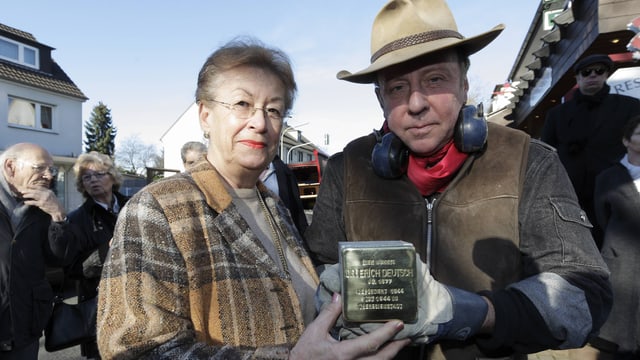 Deming und eine Frau halten einen Stolperstein in die Kamera Deming und eine Frau halten einen Stolperstein in die Kamera