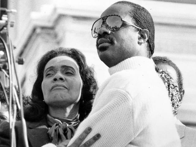 Stevie Wonder hält die Witwe von Martin Luther King im Arm. Sie trägt ein Halstuch und er einen weissen Pullover.