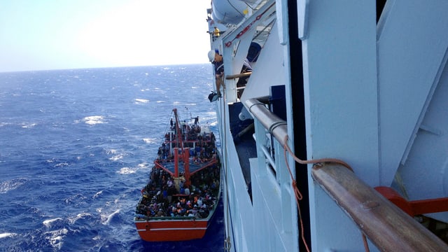 Kleines Boot, daneben Schiff. Leute im Boot. Kleines Boot, daneben Schiff. Leute im Boot.