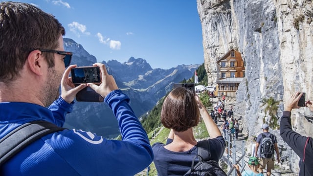 Wandertouristen fotografieren das spektakulär gelegene Restaurant Aescher im Alpstein. Wandertouristen fotografieren das spektakulär gelegene Restaurant Aescher im Alpstein.
