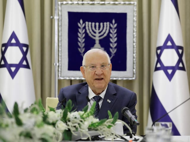Älterer Herr (Reuven Rivlin) spricht flankiert von israelischen Flaggen Älterer Herr (Reuven Rivlin) spricht flankiert von israelischen Flaggen