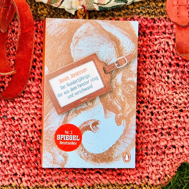 Der Schelmenroman «Der Hundertjährige, der aus dem Fenster stieg und verwand» von Jonas Jonasson liegt auf einer Beuteltasche Der Schelmenroman «Der Hundertjährige, der aus dem Fenster stieg und verwand» von Jonas Jonasson liegt auf einer Beuteltasche