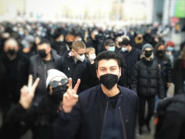 Fabian Molina mit schwarzer Maske macht an der Demo das V-Zeichen.