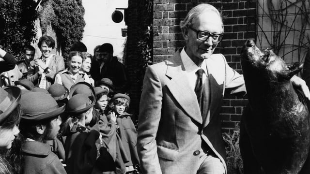 Ein älterer Mann steht neben einer Bärenstatue. Um ihn herum Kinder, die zuschauen. Ein älterer Mann steht neben einer Bärenstatue. Um ihn herum Kinder, die zuschauen.