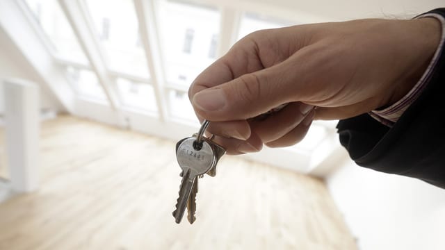 Hand hält Schlüssel vor nigelnagelneuer leerer Wohnung Hand hält Schlüssel vor nigelnagelneuer leerer Wohnung