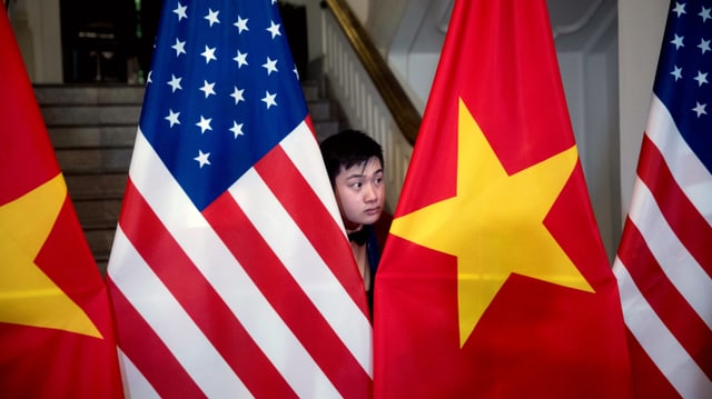 Ein Vietnamese steht zwischen der amerikanischen und der vietnamesischen Flagge. Ein Vietnamese steht zwischen der amerikanischen und der vietnamesischen Flagge.