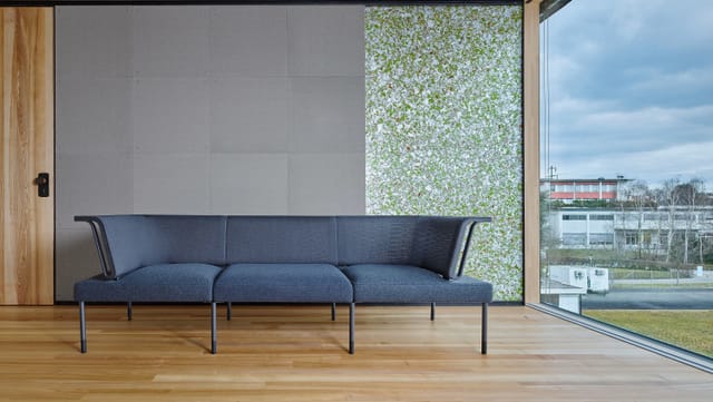ein Sofa, das in einem offenen Wohnzimmer mit grosser Fensterwand und recyclebaren Wänden steht ein Sofa, das in einem offenen Wohnzimmer mit grosser Fensterwand und recyclebaren Wänden steht