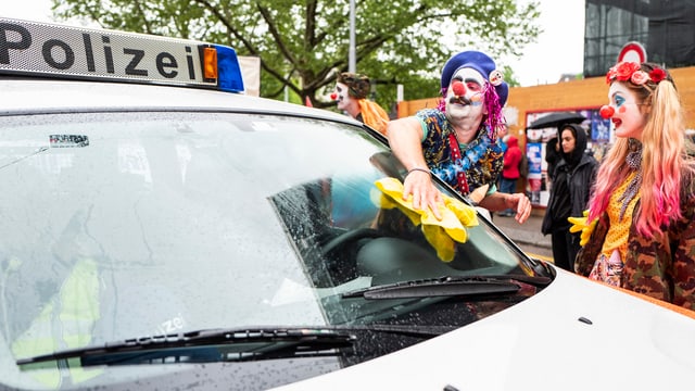 Clowns putzen die Frontscheibe eines Polizeiautos Clowns putzen die Frontscheibe eines Polizeiautos