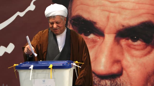 Rafsandschani, ein Mann mit weissem Turban, wirft den Stimmzettel in die Plastikurne, hinter ihm ein grosses Wandbild von Ajatollah Chomeini. Rafsandschani, ein Mann mit weissem Turban, wirft den Stimmzettel in die Plastikurne, hinter ihm ein grosses Wandbild von Ajatollah Chomeini.