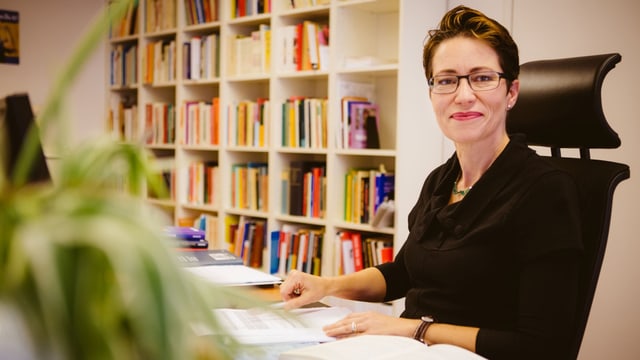 Eine Frau sitzt lächelnd an einem Schreibtisch. Eine Frau sitzt lächelnd an einem Schreibtisch.