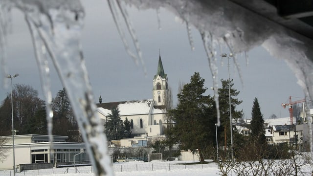 Durch Eiszapfen hindurch ist eine schneebedeckte Kirche zu sehen. Durch Eiszapfen hindurch ist eine schneebedeckte Kirche zu sehen.