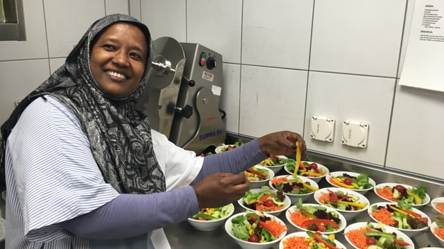 Eine Frau mit Kopftuch bereitet in einer Küche Salatportionen zu. Eine Frau mit Kopftuch bereitet in einer Küche Salatportionen zu.