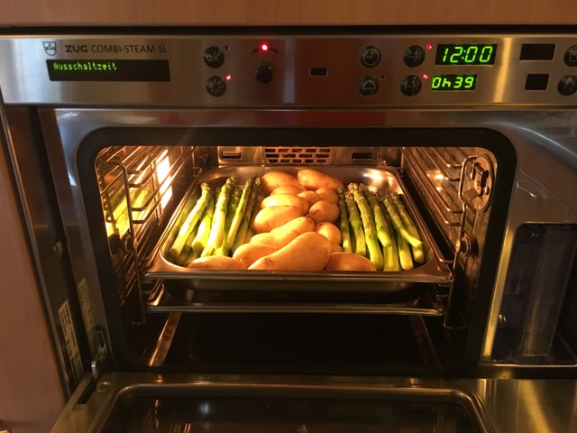 In einem Steamer liegt ein Backblech mit Spargeln und Kartoffeln. In einem Steamer liegt ein Backblech mit Spargeln und Kartoffeln.