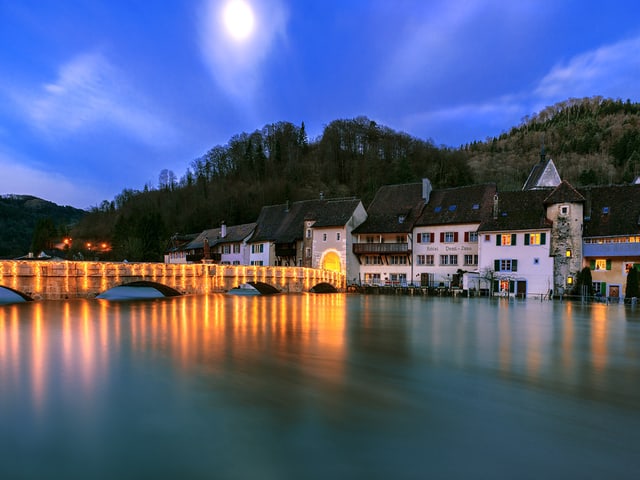 Blick auf die Altstadt mit dem Fluss im Vordergrund. Am Himmel der untergehende Mond.