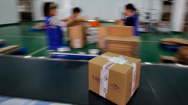 Ein Paket zeiht auf einem Band an drei Chinesischen Packerinnen vorbei. Ein Paket zeiht auf einem Band an drei Chinesischen Packerinnen vorbei.