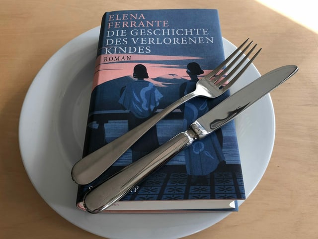 Das Buch «Die Geschichte des verlorenen Kindes» von Elena Ferrante liegt auf einem weissen Teller. Messer und Gabel nebeneinander darüber.