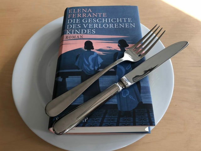 Das Buch «Die Geschichte des verlorenen Kindes» von Elena Ferrante liegt auf einem weissen Teller. Messer und Gabel nebeneinander darüber. Das Buch «Die Geschichte des verlorenen Kindes» von Elena Ferrante liegt auf einem weissen Teller. Messer und Gabel nebeneinander darüber.