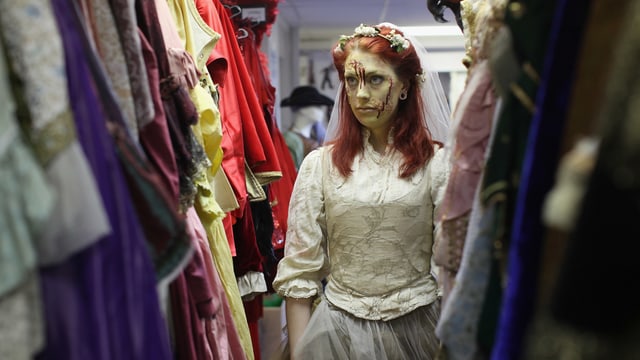 Eine Dame im Brautkleid mit künstlichem Blut im Gesicht steht zwischen Kostümen Eine Dame im Brautkleid mit künstlichem Blut im Gesicht steht zwischen Kostümen