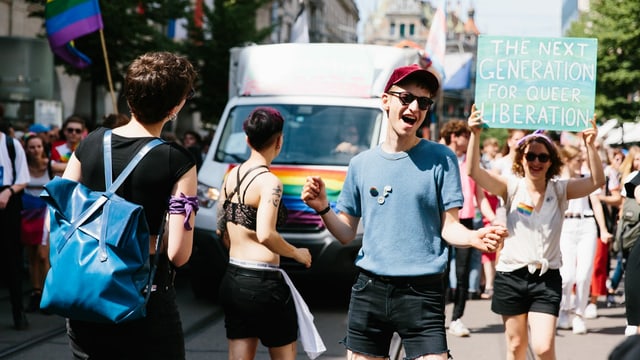 mehrere junge Menschen tanzen und halten Plakate hoch und Regenbogen-Flaggen mehrere junge Menschen tanzen und halten Plakate hoch und Regenbogen-Flaggen