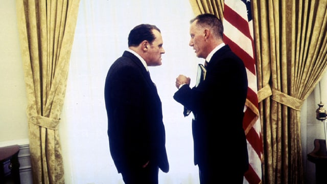 Anthony Hopkins steht als Nixon vor einem grossen Fenster seinem Stabschef Haldeman gegenüber. Im Hintergrund steht die amerikanische Flagge. Anthony Hopkins steht als Nixon vor einem grossen Fenster seinem Stabschef Haldeman gegenüber. Im Hintergrund steht die amerikanische Flagge.