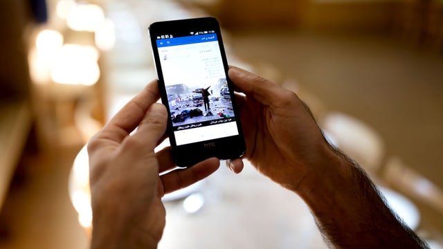 Zwei Hände halten ein Handy mit Facebook auf dem Screen.