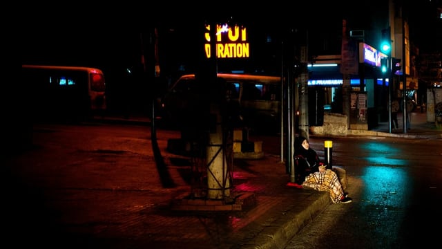 Obdachlose Frau in der Dunkelheit, sie sitzt am Strassenrand. Obdachlose Frau in der Dunkelheit, sie sitzt am Strassenrand.