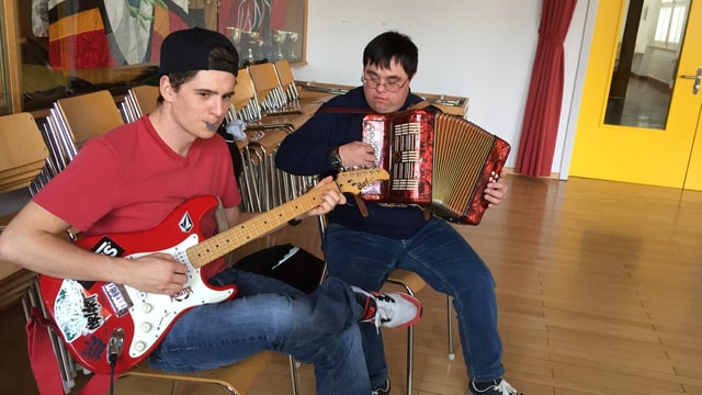Ein junger Mann spielt Gitarre, daneben ein anderer Mann an der Handorgel. Ein junger Mann spielt Gitarre, daneben ein anderer Mann an der Handorgel.