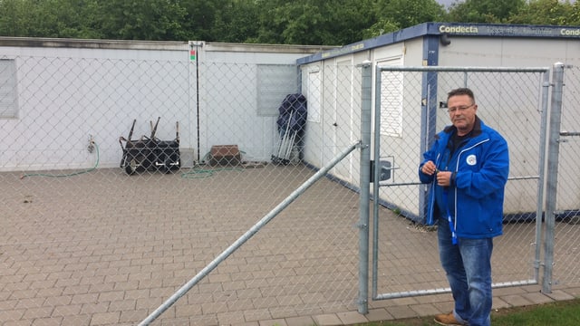 Mann öffnet ein Gitter. Im Hintergrund ist eine Container-Siedlung zu erkennen. Mann öffnet ein Gitter. Im Hintergrund ist eine Container-Siedlung zu erkennen.