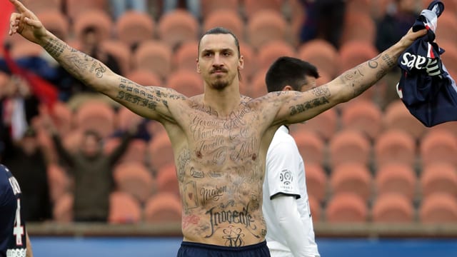 Zlatan Ibrahimovic mit nacktem Oberkörper, die Hände ausgestreckt und mit zahlreichen Tattoos auf seinem Oberkörper.