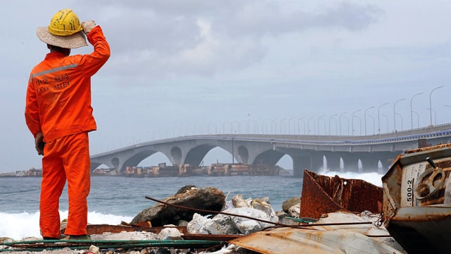 Ein Arbeiter in orangem Gewand steht vor der Brücke in der Ferne. Ein Arbeiter in orangem Gewand steht vor der Brücke in der Ferne.