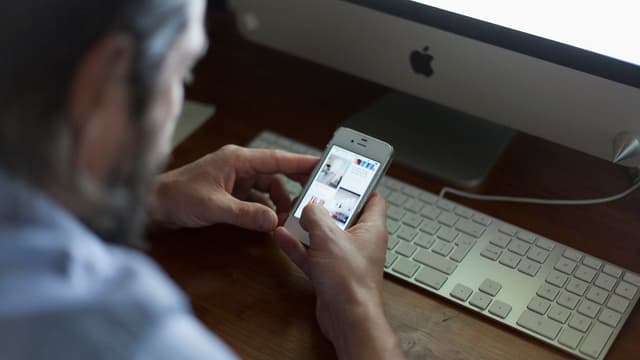 Mann mit Smartphone vor einem Computer. Mann mit Smartphone vor einem Computer.