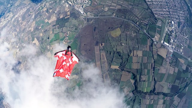Ein Mann im Wingsuit-Anzug fliegt. Unter ihm sind Felder und Städte sichtbar. Ein Mann im Wingsuit-Anzug fliegt. Unter ihm sind Felder und Städte sichtbar.