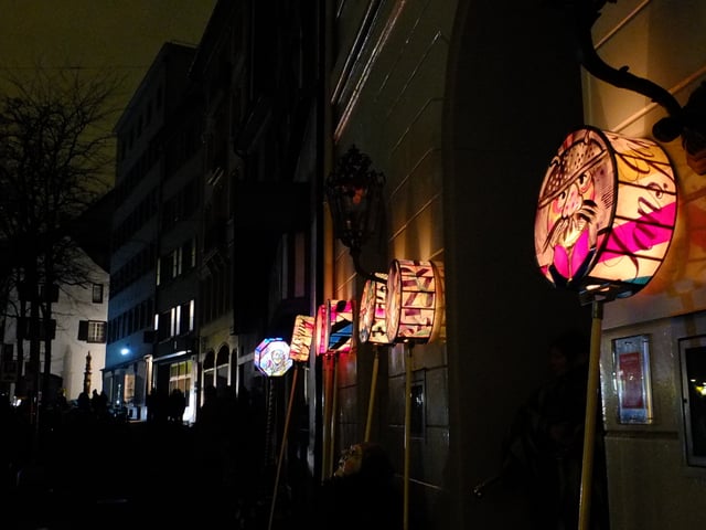 An Häuserfassade aufgereihte Stablaternen.