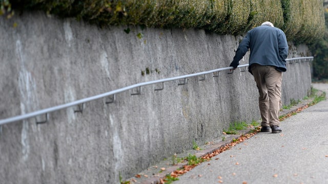 Ein älterer Mann läuft auf einem Gehsteig entlang eines Geländers. Ein älterer Mann läuft auf einem Gehsteig entlang eines Geländers.