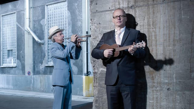 Schertenlaib spielt Ukulele während Jegerlehner mit der Trompete gegen die Wand spielt Schertenlaib spielt Ukulele während Jegerlehner mit der Trompete gegen die Wand spielt