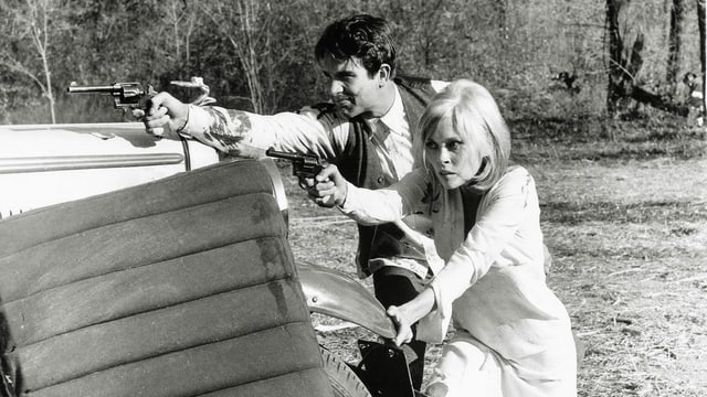 Eine Frau und eine Mann stehen hinter einem Auto. Beide haben eine Waffen in der Hand und schiessen in die selbe Richtung. Eine Frau und eine Mann stehen hinter einem Auto. Beide haben eine Waffen in der Hand und schiessen in die selbe Richtung.