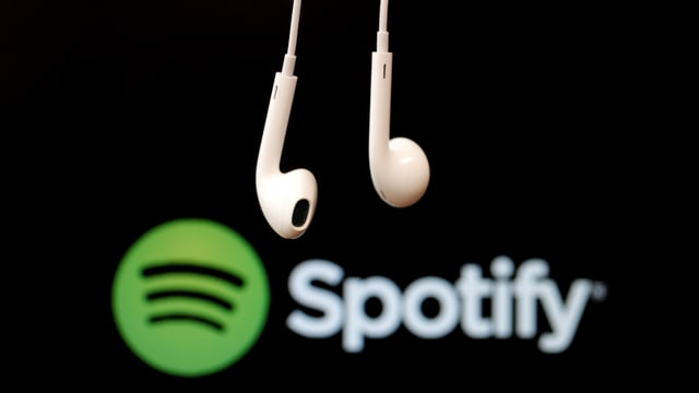 Ein Paar Kopfhörer vor dem Spotify-Logo. Ein Paar Kopfhörer vor dem Spotify-Logo.