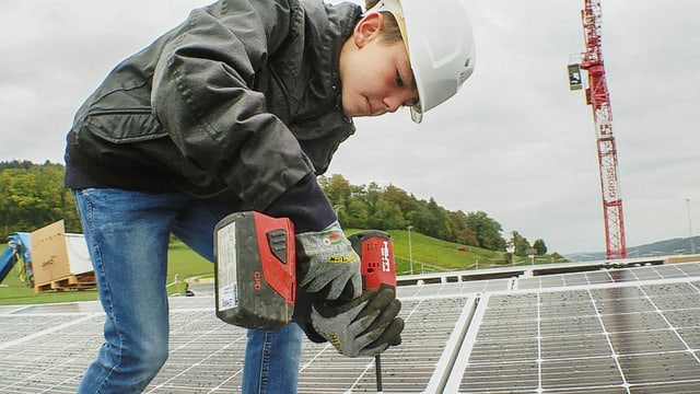 Ein Junge mit Helm und einer Bohrmaschine befestigt Solarzellen. Ein Junge mit Helm und einer Bohrmaschine befestigt Solarzellen.