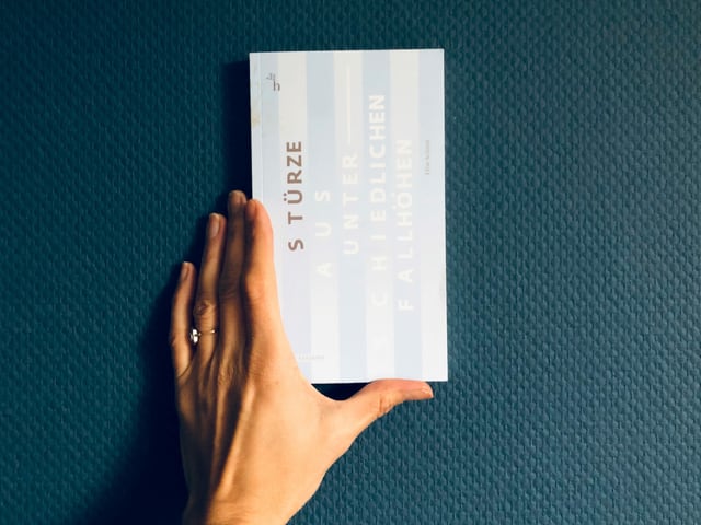 Der Erzählband «Stürze aus unterschiedlichen Fallhöhen» von Elise Schmit vor einer blauen Tapetenwand Der Erzählband «Stürze aus unterschiedlichen Fallhöhen» von Elise Schmit vor einer blauen Tapetenwand